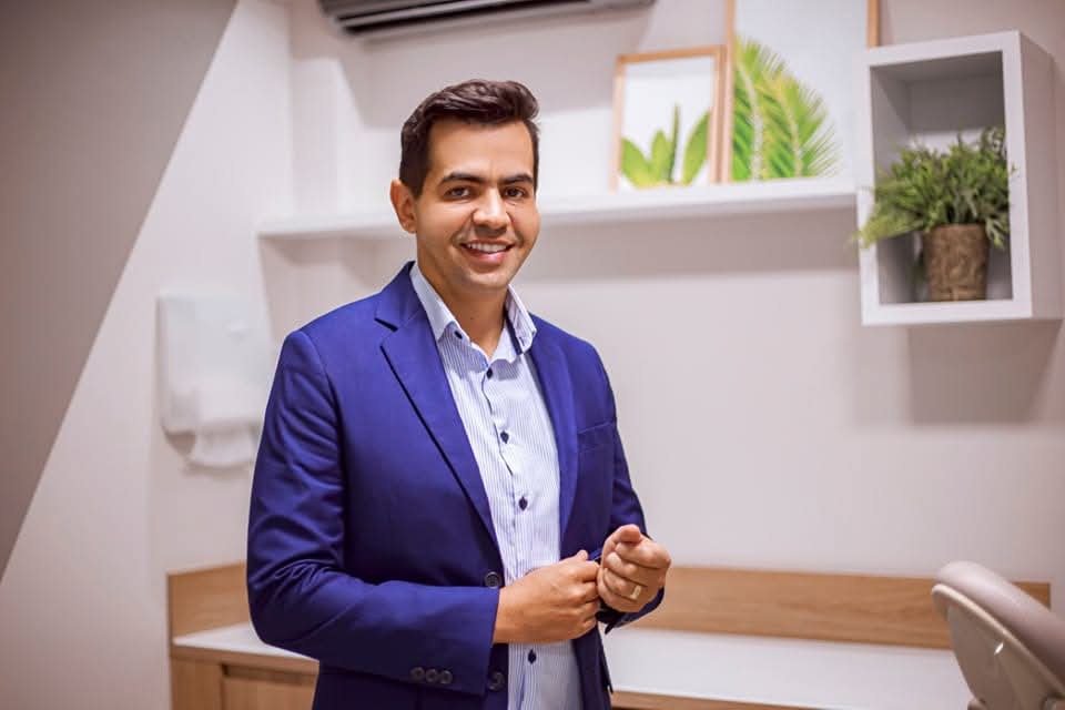 André Romano em pé no consultório, pronto para atender